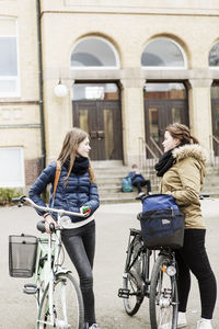 Schoolgirls with bicycles talking outside school building