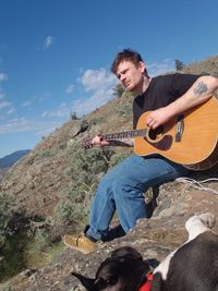 Man playing guitar on mountain against sky