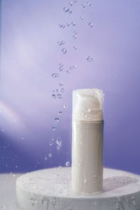 Cosmetic bottle with water splashes on a purple background.