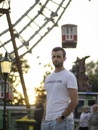 Portrait of young man standing in city with a fair ferris wheel