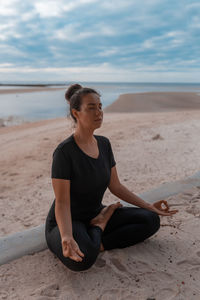 Side view of woman sitting at beach against sky