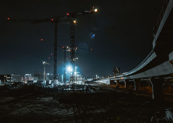 Illuminated railroad tracks in city against sky at night