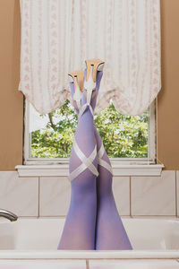 Low section of woman standing by window at home