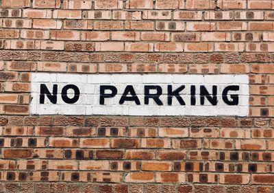 Close-up of no parking sign on brick wall