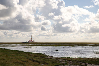 View of lighthouse by sea against cloudy sky