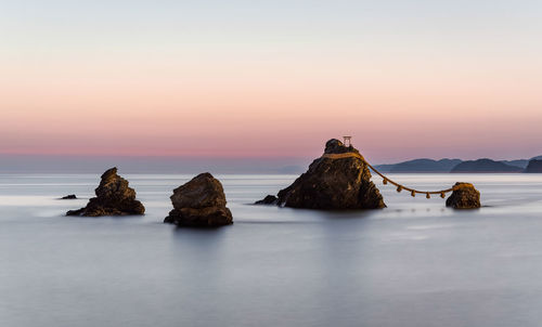 Rocks in sea against sky during sunset