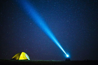 Silhouette person with illuminated headlamp camping against star field