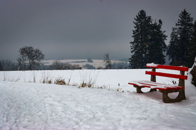 Empty bench on snow covered field against sky