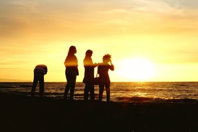 Silhouette people standing on beach against sky during sunset