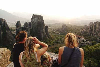 Rear view of women sitting on rock against mountains