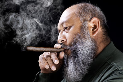 Close-up of man smoking cigar against black background