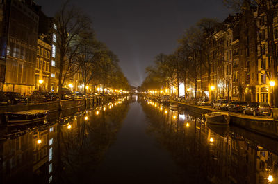 Canal amidst illuminated buildings in city at night