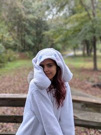 Portrait of young woman wearing white warm clothing while standing against trees