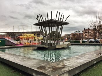 Ferris wheel by sea against sky in city