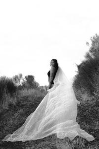 Portrait of woman wearing wedding dress standing on field