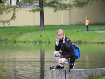 Full length portrait of girl crouching by lake