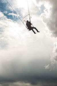 Low angle view of man hanging on rope against sky