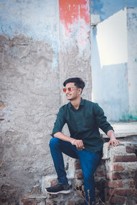 Young man looking away while standing against wall