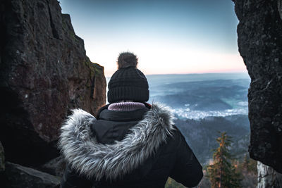 Rear view of woman standing on rock against sky during winter