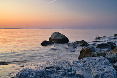 Rocks in sea against sky during sunset