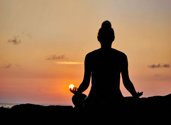 Rear view of silhouette man sitting against orange sky