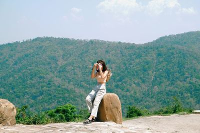 Full length of man sitting on mountain against sky