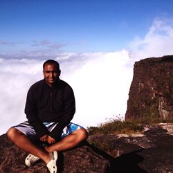 Portrait of mid adult man sitting on mt roraima against cloudy sky