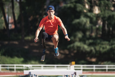 Young athlete with prosthetic leg jumping above railings at running track