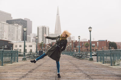 Woman dancing on bridge against buildings in city