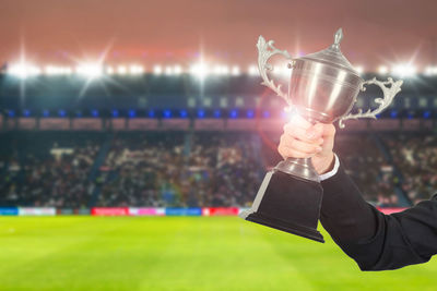 Cropped hand of businesswoman holding trophy at stadium