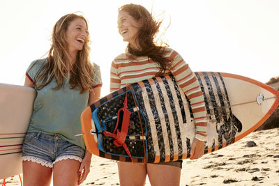 Two happy women carrying surfboards on the beach