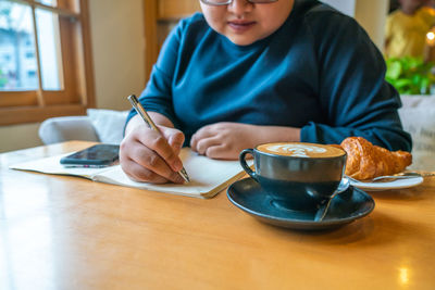 Midsection of woman writing in notebook in cafe