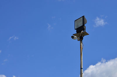 Low angle view of security camera on floodlight against blue sky