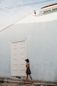 Woman in hat walking against house