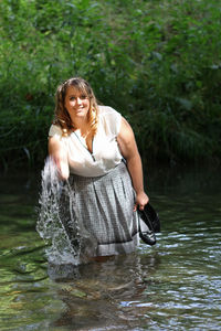 Young woman splashing water while standing in river against plants