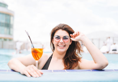 Stylish woman plus size body positive in black swimsuit with glass of cocktail in pool