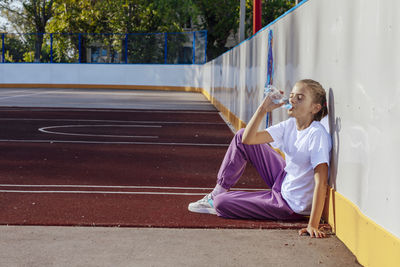 Girl drinks water while sitting on a rubber coating on the basketball court. sport, active lifestyle 