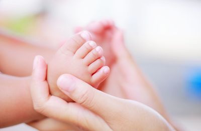 Cropped hands of woman holding baby feet at home