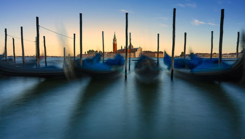 Boats moored by wooden post on canal against sky during sunset