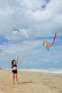 Rear view of woman with arms outstretched standing at beach against sky