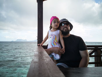 Man with daughter by railing against sea