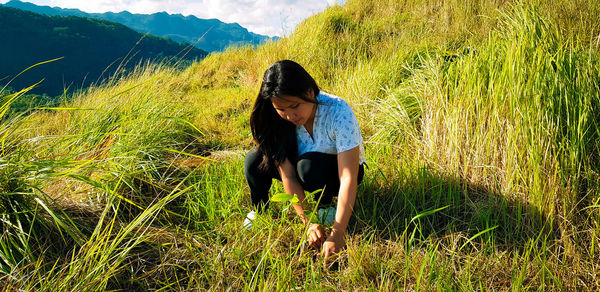 Young woman picking grass while crouching on field