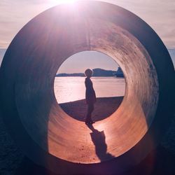 Side view of woman standing in pipe at beach on sunny day