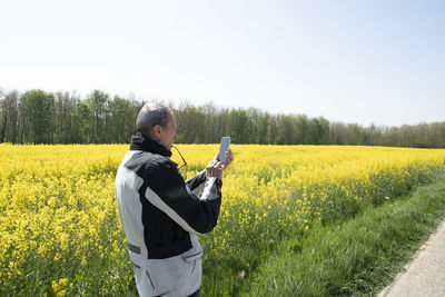 A middle-aged man motorcyclist stands on field flowering yellow rapeseed