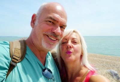 Close-up portrait of smiling mature couple at beach during sunny day