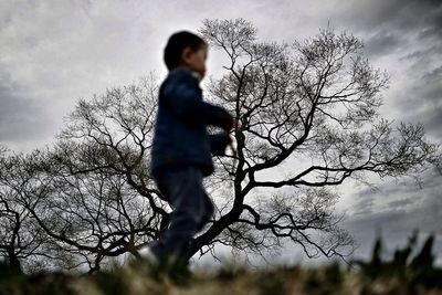 Rear view of boy standing on field against sky