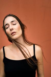 Close-up of young woman against coral background