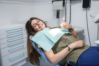 Portrait of smiling young woman showing thumbs up on dentist chair