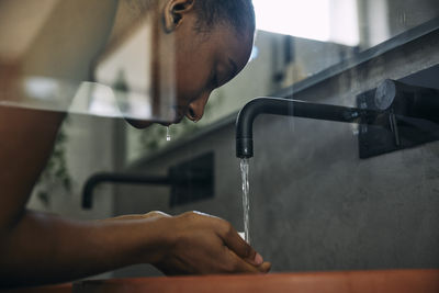 Low angle view of woman washing face with faucet water in bathroom