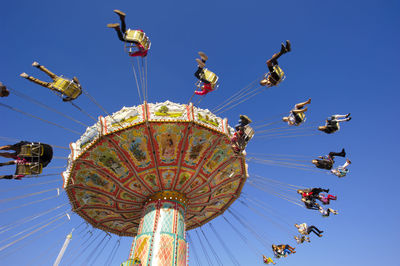 Low angle view of people on chain swing ride against clear blue sky